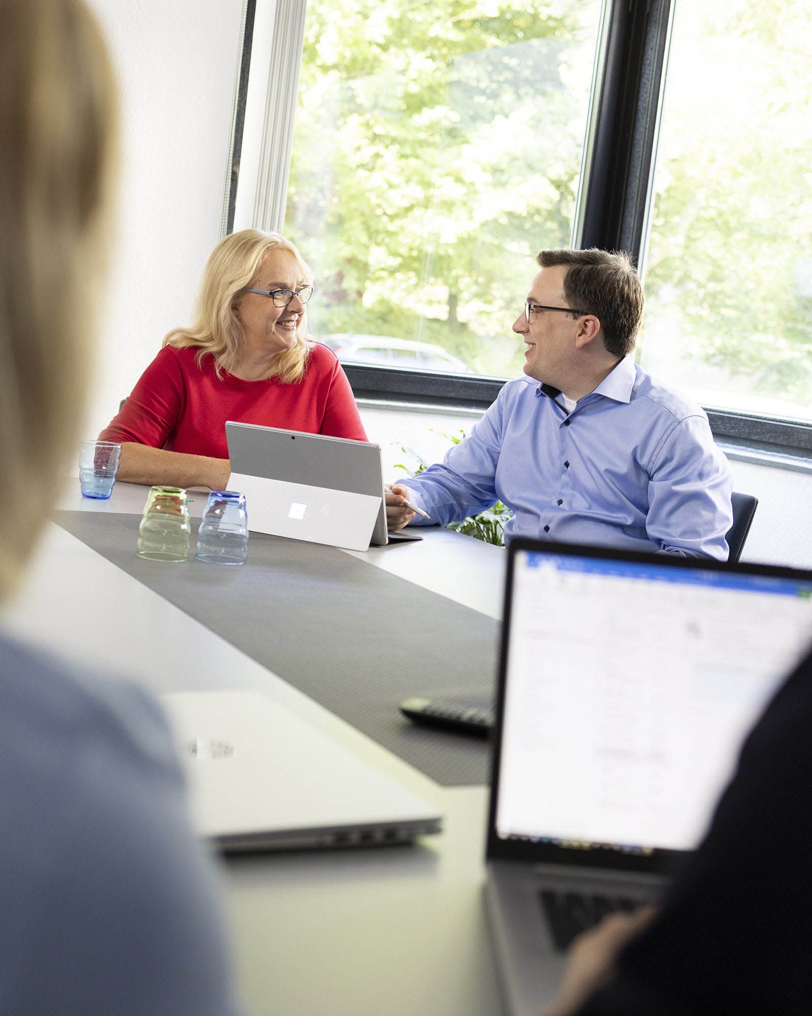 Frau Vox und Herr Beusker sitzen am Tisch in einer Besprechung und schauen sich gegenseitig an